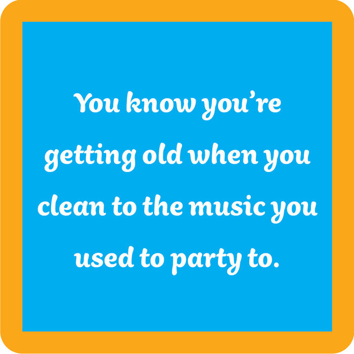 A blue square with a yellow-orange border features the Clean to Music Coaster by Drinks On Me, printed with "You know you’re getting old when you clean to the music you used to party to"—a funny drink coaster or quirky bar cart accessory.