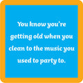 A blue square with a yellow-orange border features the Clean to Music Coaster by Drinks On Me, printed with "You know you’re getting old when you clean to the music you used to party to"—a funny drink coaster or quirky bar cart accessory.