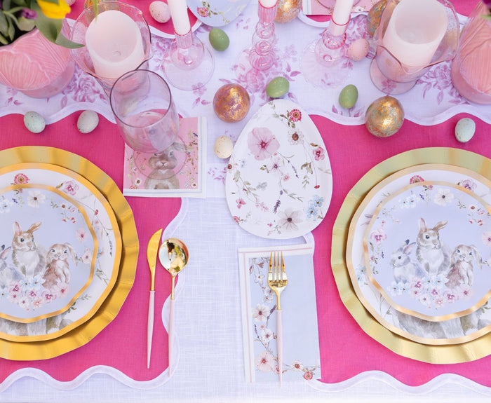 Create a festive Easter setting with the Ultimate Easter Tablescape for 16: Charming Easter by Sophistiplate LLC, featuring pink placemats, gold utensils, rabbit-themed designer plates, decorative eggs, candles, and floral accents.
