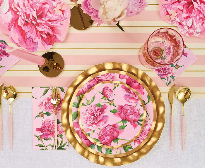 A table setting with Sophistiplate Cocktail Napkin Pink Peonies (26/pkg), pink floral plates, gold charger, pink and gold cutlery, a striped runner, and vases of peonies creates a vibrant, elegant look.