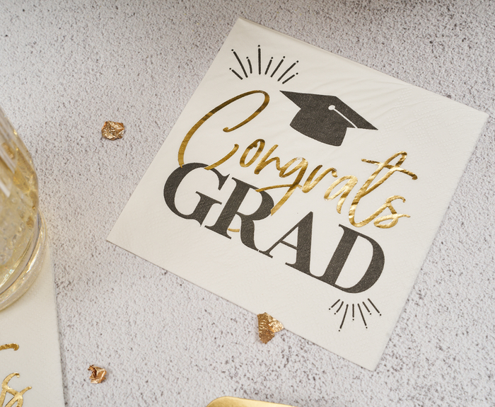 Celebrate graduation with Sugarplum’s Congrats Grad Cocktail Napkins (26pk), featuring white napkins with gold and black “Congrats GRAD” text and a black cap—ideal for stylish grad party displays.