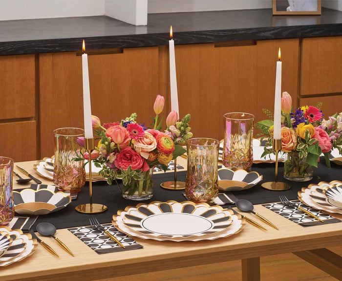 The Cordoba Table Setting by Sophistiplate LLC features designer disposable plates, gold flatware, floral accents, candles in gold holders, and patterned napkins for an elegant, festive dining ambiance.