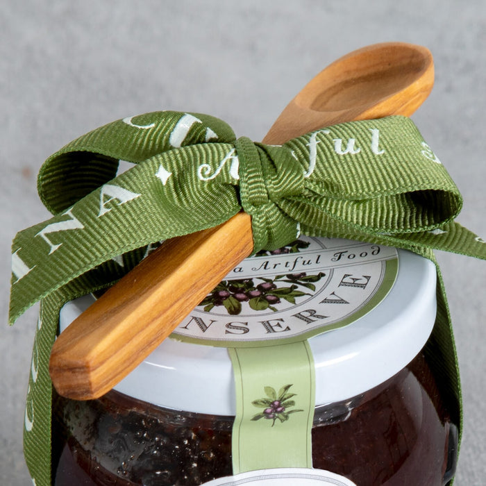 Bella Cucina Cranberry Conserve Gift w/ Spoon features a jar adorned with a green bow, wooden spoon on top, and an olive branch label—an ideal sweet-tart Thanksgiving condiment.