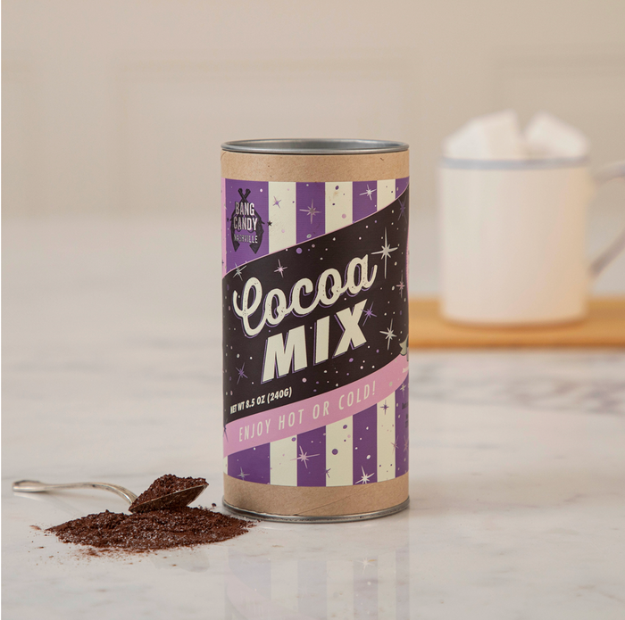 A Bow Mug + Hot Cocoa Gift Set by Sophistiplate LLC sits on a marble counter, featuring a retro-labeled cocoa mix canister and a mug filled with marshmallows—perfect for gifting or enjoying yourself.