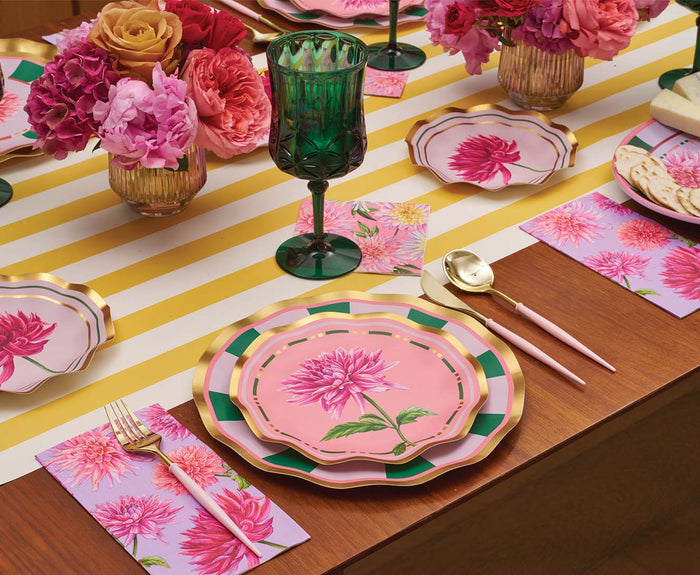 A table set with pink floral plates, matching napkins, gold flatware with pink handles, green goblets, and vases of pink and orange flowers on a yellow-striped table runner is completed by charming Sophistiplate Dahlia Garden Appetizer/Dessert Bowls (8pk)—perfect for serving appetizers in style.
