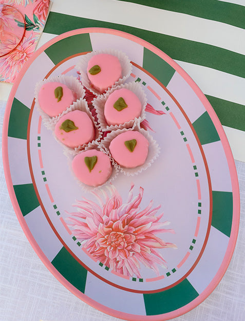 The Sophistiplate Dahlia Garden Melamine Serving Platter holds six pink heart-shaped treats with green toppers in white paper cups, displayed on a table with striped and floral patterns.