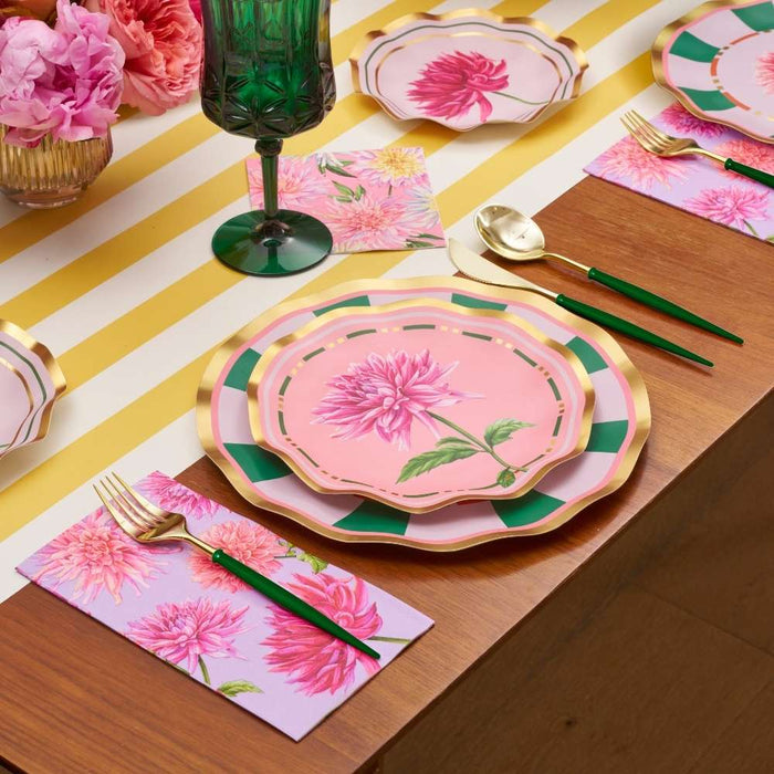 The Dahlia Garden Table Setting by Sophistiplate LLC features floral pink designer plates, gold-rimmed green-handled cutlery, a green glass, yellow and white striped runner, pink napkins, and floral centerpieces for a charming look.