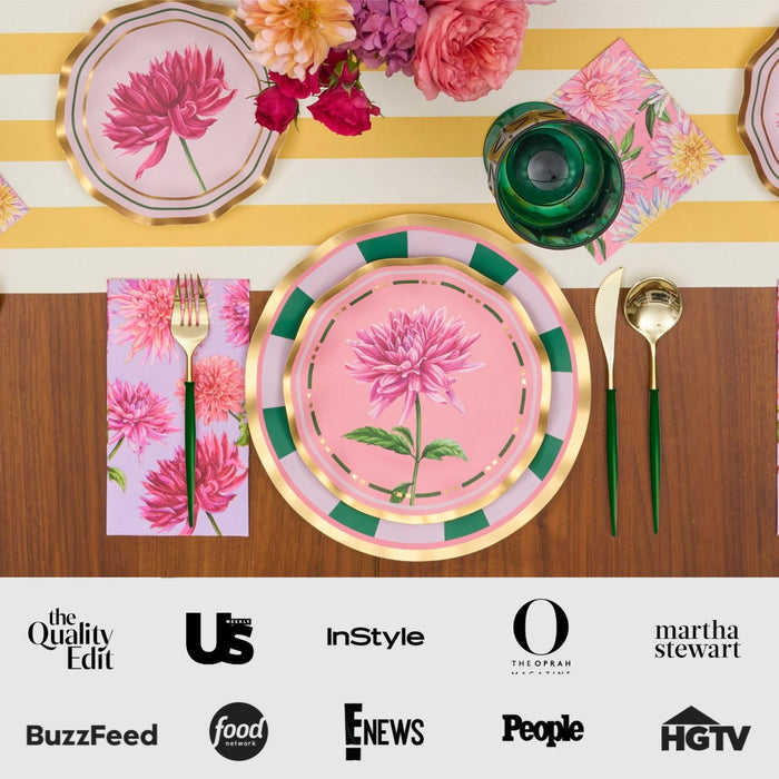 The Dahlia Garden Table Setting by Sophistiplate LLC features designer disposable plates with pink florals, green and gold cutlery, a green glass, matching napkins, and a striped yellow and white tablecloth. Media logos appear along the bottom.