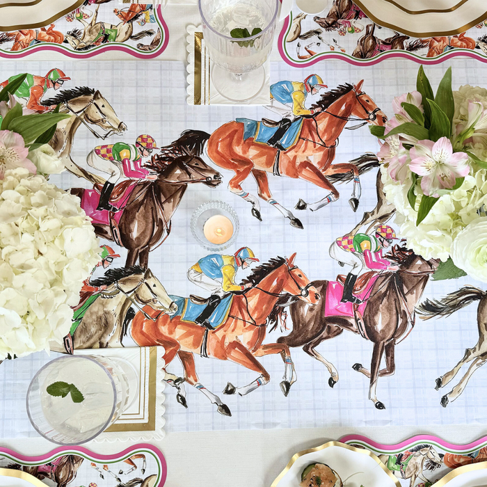 A decorative table is set with illustrated placemats, a Rosanne Beck Derby Racehorses Table Runner (20x12"), white hydrangeas, pink blooms, glassware, and a lit tealight candle.