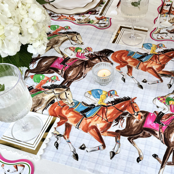 A decorated table with the Rosanne Beck Derby Racehorses Table Runner (20x12"), clear glassware, a candle, white hydrangeas, and horse-themed placemats creates an elegant equestrian-inspired dining scene.