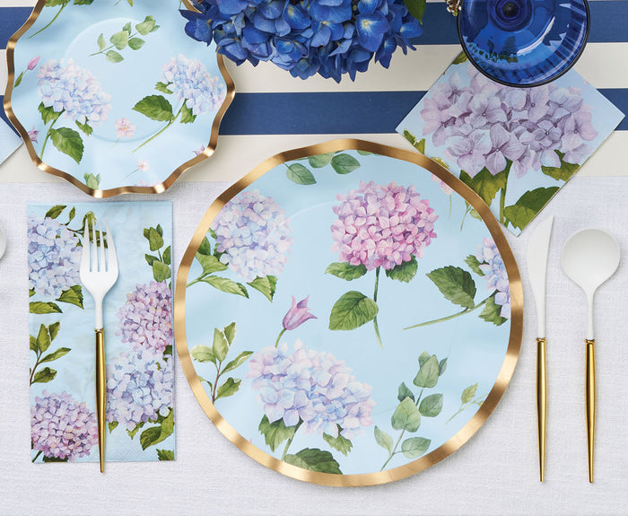 The Sophistiplate Hydrangea Table Setting includes designer disposable plates with blue and purple hydrangeas, gold-rimmed cutlery, a blue and white striped tablecloth, matching napkins, and blue floral accents for an elegant party-in-a-box.