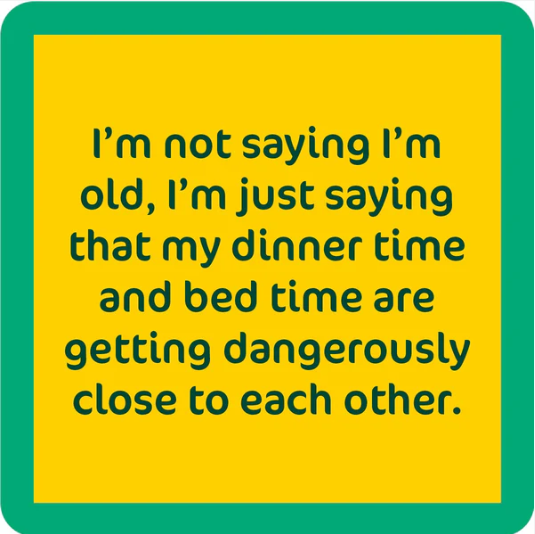 The Drinks On Me Dinner Time Coaster features a yellow square with a green border and the text: "I’m not saying I’m old, I’m just saying my dinner time and bed time are getting dangerously close"—a perfect quirky gift or funny drink coaster.