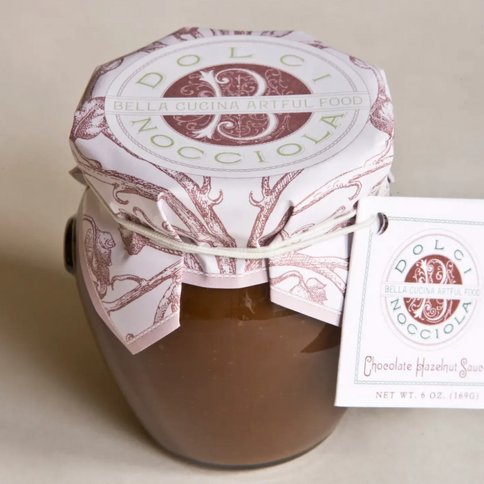 A 6 oz glass jar of Bella Cucina Dolci Nocciola Hazelnut Sauce, elegantly wrapped and tagged, offers pure Italian chocolate hazelnut flavor in every spoonful.