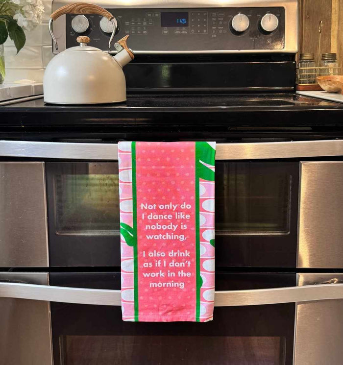 A Drinks On Me "Don't work in Morning Dish Towel" hangs from the oven handle under a tea kettle—a pink and green towel with a humorous quote, perfect as a funny housewarming gift.