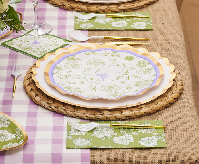 Create a spring-themed Easter tablescape with the Ultimate Easter Tablescape for 16: Easter Toile by Sophistiplate LLC, featuring woven placemats, bunny and floral scalloped plates, gold/white cutlery, green floral napkins, and a pink gingham tablecloth.