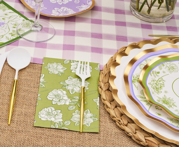 Create a festive Easter setting with the Sophistiplate LLC Ultimate Easter Tablescape for 16: Easter Toile—gold and purple-trimmed plates, green floral napkins, white plastic cutlery, woven placemats, and a purple plaid tablecloth with flowers overhead.