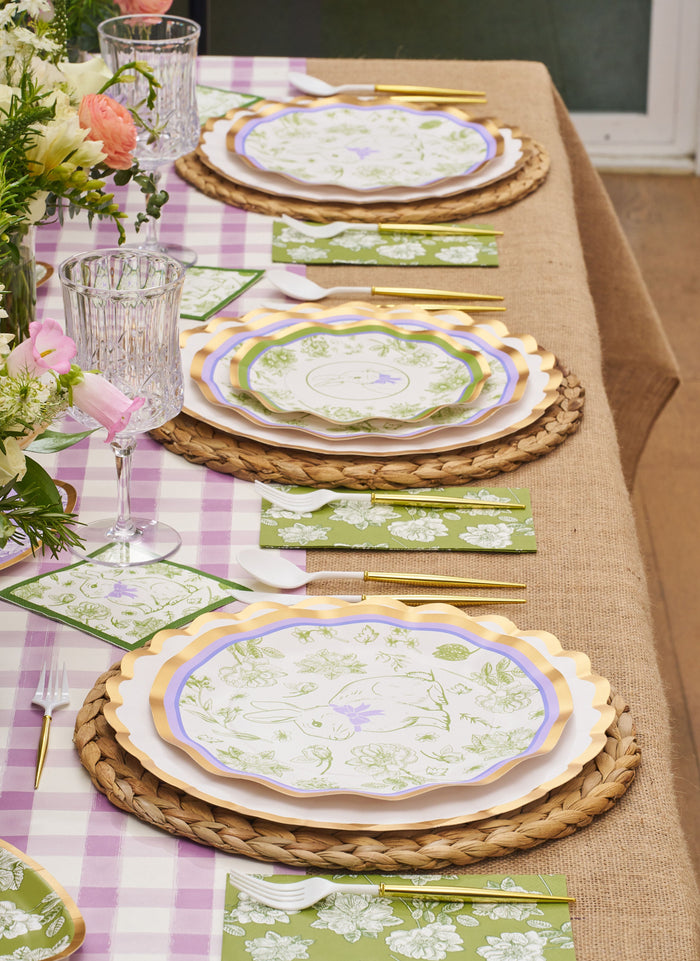 The Ultimate Easter Tablescape for 16: Easter Toile by Sophistiplate LLC features designer paper plates, gold cutlery, crystal glasses, floral napkins, placemats, and a pink gingham tablecloth—perfect for a festive setting.