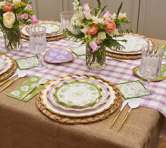 The Ultimate Easter Tablescape for 16: Easter Toile by Sophistiplate LLC includes floral designer plates, gold flatware, green napkins, crystal glasses, and flower centerpieces on a purple gingham and burlap tablecloth.