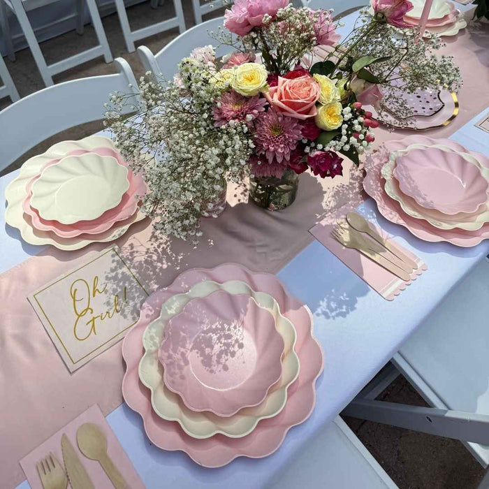 The Sophistiplate LLC Eco Cream & Blush Table Setting for 16 features pink and cream designer plates, gold cutlery, a matching table runner, and floral accents—perfectly arranged for celebrations.