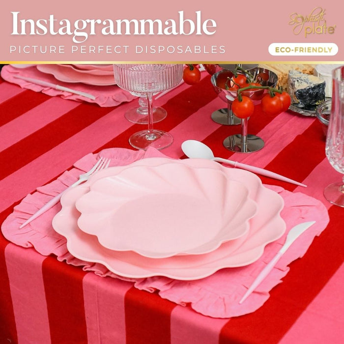 A table set with Sophistiplate’s Eco-Friendly Table Setting-Blush: pink shell-shaped plates, matching cutlery, crystal glasses on a red and pink striped cloth. A sign reads "Instagrammable Picture Perfect Disposables, Eco-Friendly.