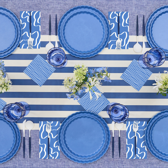 The Sophistiplate Eco-Friendly Table Setting-French Blue features blue plates and glasses, white cutlery, patterned napkins, a striped runner, and floral centerpieces for six—perfect for a chic blue and white tablescape.
