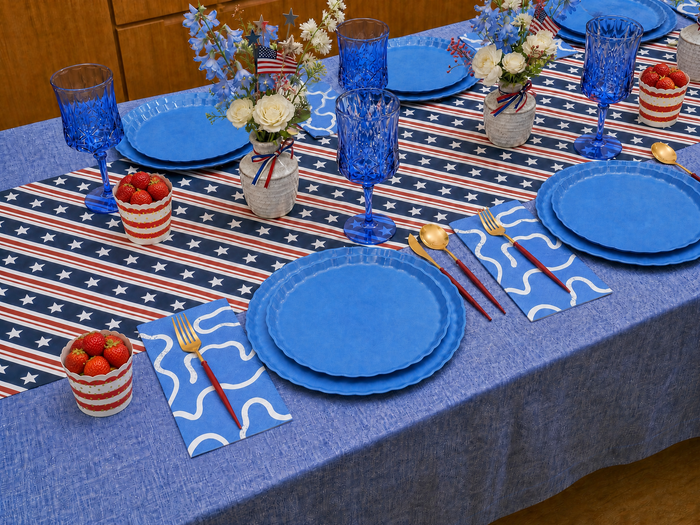 Create a festive 4th of July table for 16+ with Sophistiplate LLC’s French Blue Party Pack, featuring eco-friendly plates, gold utensils, blue glassware, striped cups, and patriotic accents for a stylish celebration.