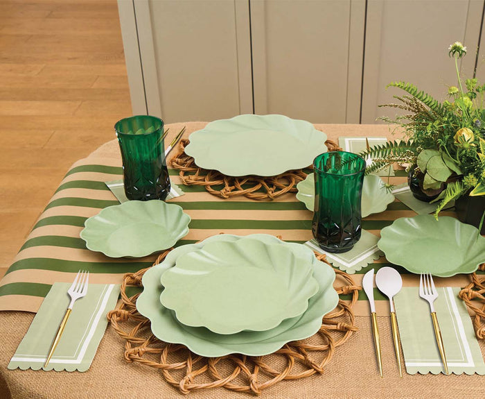 The Eco-friendly Table Setting- Sage by Sophistiplate LLC features heavy-duty bamboo plates, green-tinted glasses, striped woven placemats, gold and white cutlery, and a potted plant centerpiece for a stylish dining table.