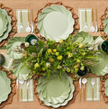 The Eco-friendly Table Setting- Sage by Sophistiplate LLC features pale green disposable plates, gold and white cutlery, green glasses, and a greenery and yellow flower centerpiece on a burlap tablecloth.