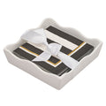 The Sophistiplate Everyday Cocktail Napkin with Napkin Tray features a wavy ceramic holder displaying stylish cocktail napkins in black, white, and gold stripes, neatly tied with a white satin ribbon.