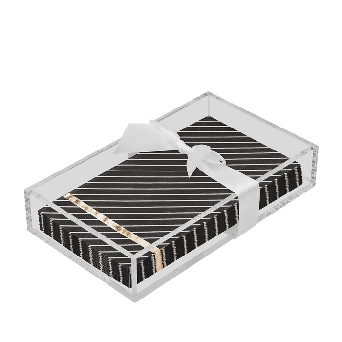 The Sophistiplate Everyday Guest Towel with Napkin Tray showcases black napkins with diagonal white stripes and gold accents in a clear rectangular holder, elegantly finished with a white ribbon tied in a bow.