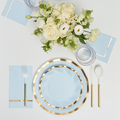 The Sophistiplate Everyday Sky Blue Table Setting includes blue and gold-rimmed designer disposable plates, gold-handled cutlery, a glass, a blue striped napkin, and a bouquet of white and cream flowers on a white background.