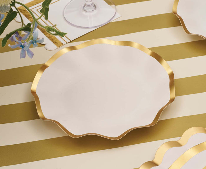 A set of Everyday White Appetizer/Dessert Bowls by Sophistiplate sits atop a striped yellow and white tablecloth, their graceful scalloped edges and gold rims echoing the style of sophisticated table settings, complemented by a nearby wine glass and fresh flowers.