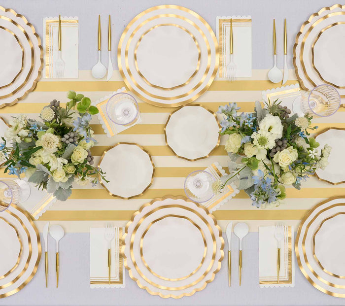 Elegant table setting with gold cutlery, striped gold and white table runner, white napkins, and floral centerpieces featuring white and light blue flowers on Sophistiplate's Everyday White Charger Plates (8pk).