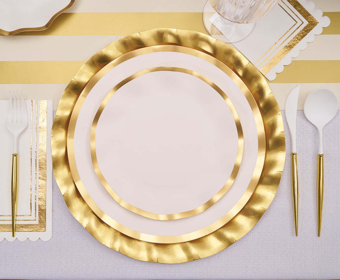 A table setting featuring Sophistiplate’s Everyday White Dinner Plates (8pk), elegantly arranged with gold and white utensils, a scalloped napkin, and a glass on a striped gold and white tablecloth.