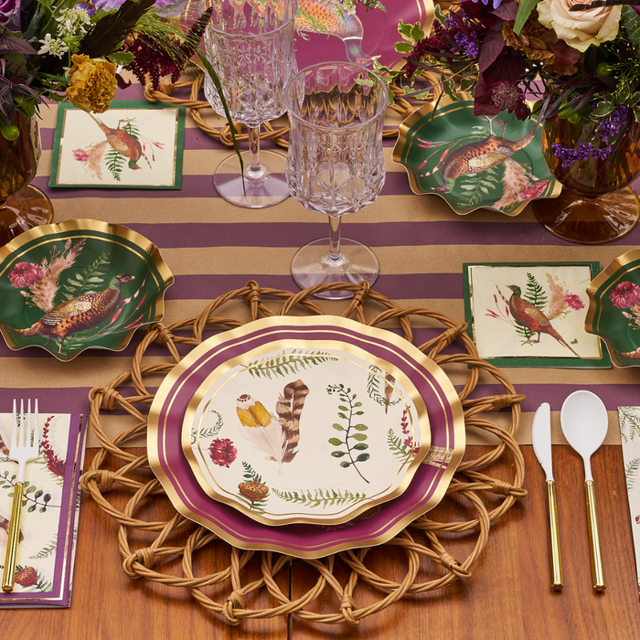 Create a stunning fall look with the Feather Grove Table Setting by Sophistiplate—botanical and feather motif plates, bird-illustrated napkins, gold utensils, and crystal glasses on a pink and gold striped tablecloth accented by floral arrangements.