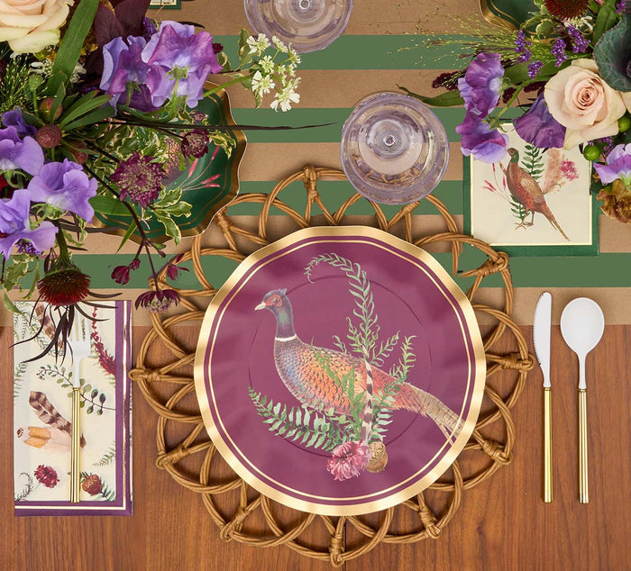 The Feather Grove Table Setting by Sophistiplate features a woven placemat, pheasant decorative plate, elegant party tableware, gold and white cutlery, floral napkins, two glasses, and floral centerpieces with purple and burgundy blooms.