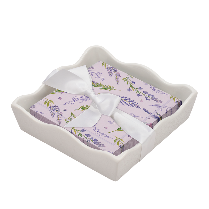 The Sophistiplate Floral Cocktail Napkin with Napkin Tray features lavender-themed napkins tied with a white ribbon in a wavy-edged ceramic tray, adding charm to any modern tabletop.