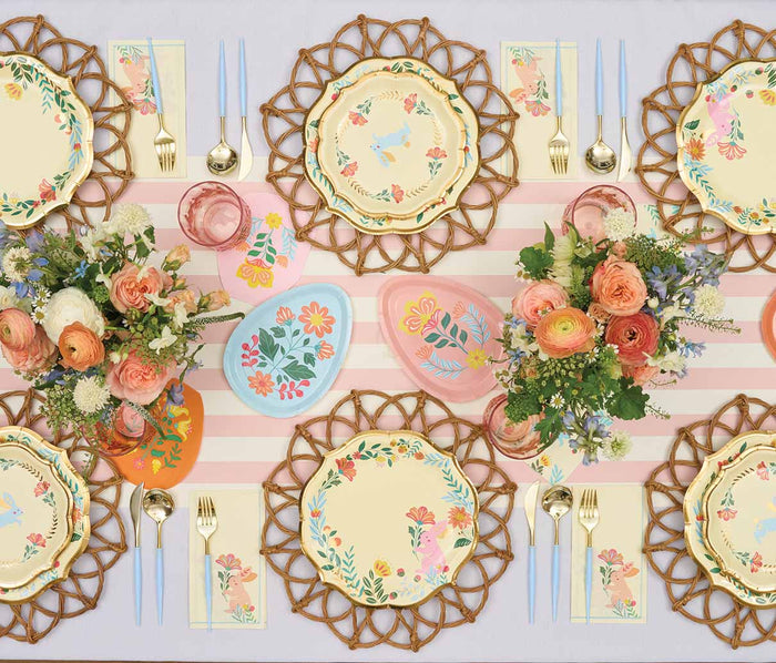 Create a charming spring Easter table for six with Sophistiplate's Folklore Easter Dinner Plates (8pk), gold utensils, pastel napkins, pink glasses, floral centerpieces, painted eggs, and a pink-and-white striped runner.