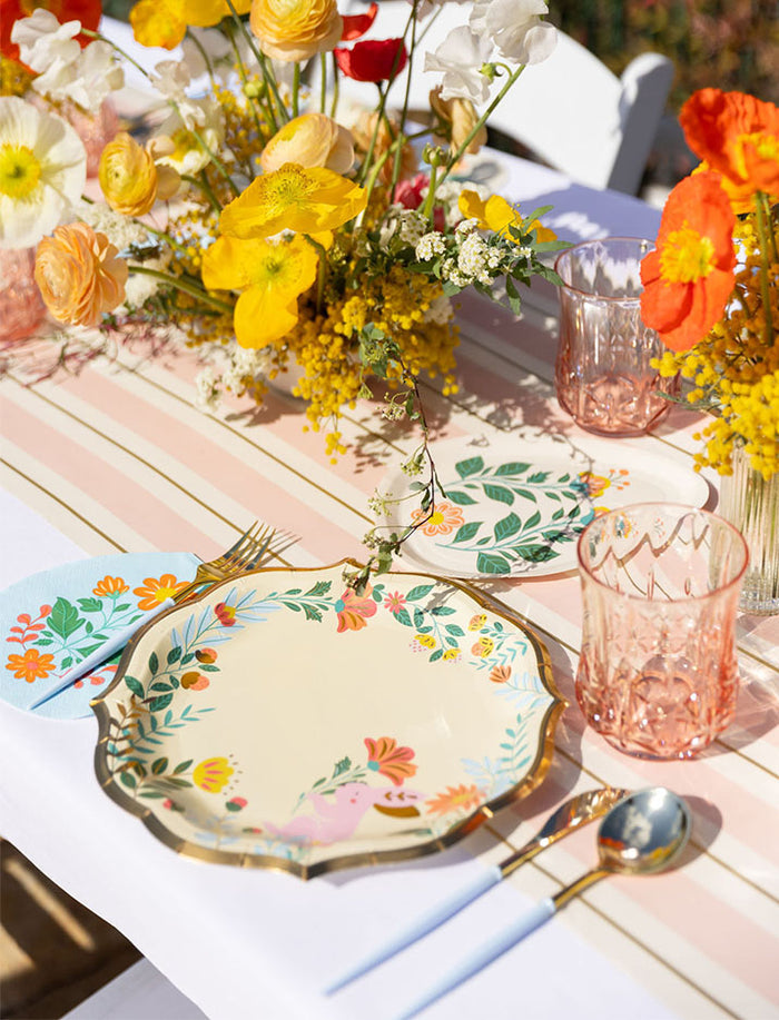 Create a bright spring tablescape with Sophistiplate LLC’s Ultimate Easter Tablescape for 16: Folklore Easter, featuring designer plates, pink glassware, gold utensils, and floral decor—perfect for outdoor gatherings.