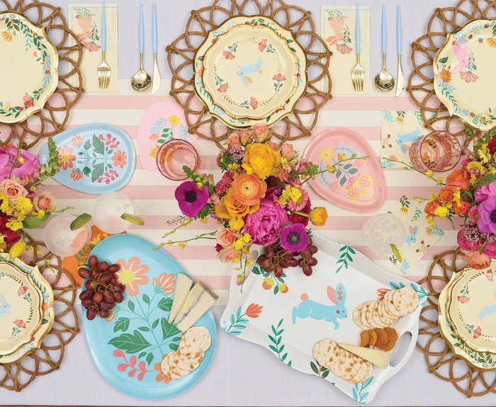 A festive spring table with floral plates, wicker placemats, pastel cutlery, and the Sophistiplate Folklore Easter Melamine Tray filled with cheese, crackers, and grapes on a pink striped tablecloth adds playful charm to your celebration.