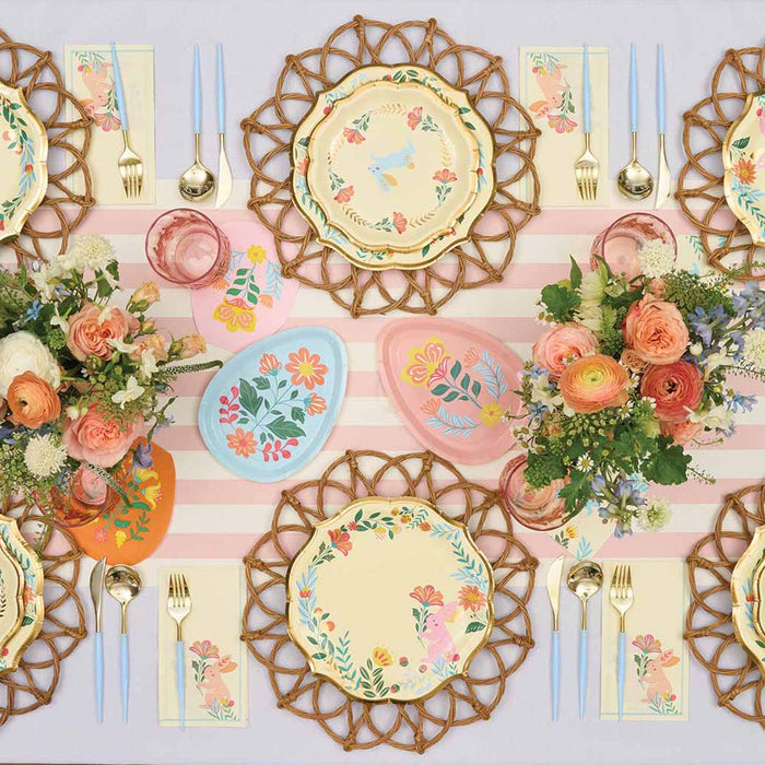 Create a cheerful spring celebration with Sophistiplate LLC's Ultimate Easter Tablescape for 16: Folklore Easter, featuring designer plates, pastel egg decor, gold utensils, a pink striped tablecloth, and floral bouquets.