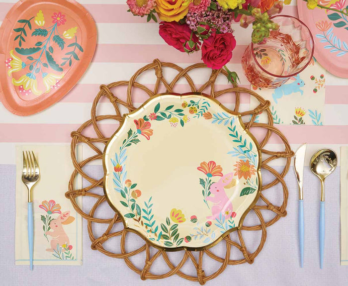 Create a charming Easter table with the Ultimate Easter Tablescape for 16: Folklore Easter by Sophistiplate LLC, featuring designer bunny plates, gold cutlery, pink floral napkins, pink-accented glasses, and a striped centerpiece.