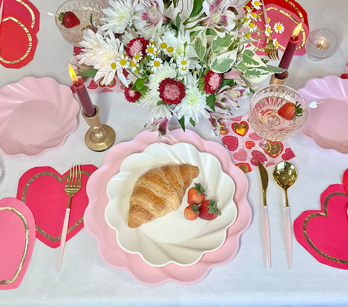The Forever Blushing Table Setting by Sophistiplate includes pink scalloped designer disposable plates, gold cutlery, heart-shaped decor, candles, a floral bouquet, and more for a festive tablescape in a box.