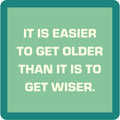 Bold white text on a light green background with a teal border reads, “IT IS EASIER TO GET OLDER THAN IT IS TO GET WISER”—a fun Drinks On Me Coaster Bundle: Birthday gift for friends or as part of a coaster set.