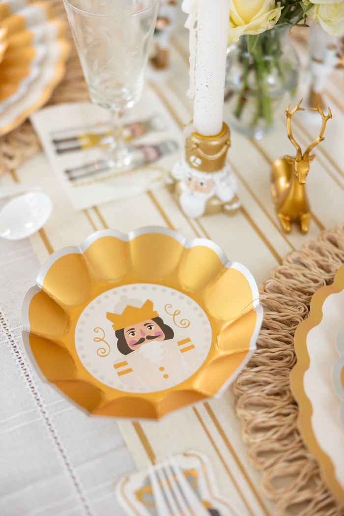 A gold and white scalloped bowl featuring a playful king design from Sophistiplate’s Gilded Nutcracker Appetizer/Dessert Bowls (8pk) adds festive flair to your holiday table, surrounded by sparkling glassware, a gold deer figurine, and a nutcracker candleholder. These charming bowls capture the spirit of special occasions with the ease and convenience of disposable tableware—making them an ideal choice for your holiday tablescape.