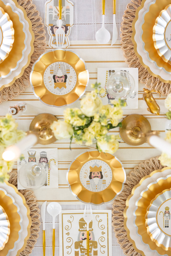 A stylish Nutcracker-themed table setting featuring Sophistiplate’s Gilded Nutcracker Appetizer/Dessert Bowls (8 pack) with decorative scalloped edges, complemented by Nutcracker-inspired napkins, gold utensils, and floral centerpieces—a festive, elegant holiday ambiance viewed from above.