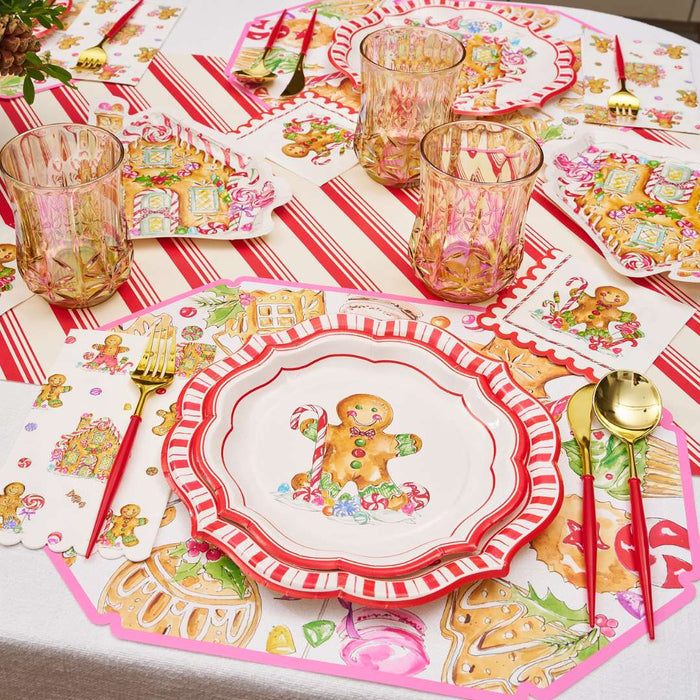 A festive Christmas table features Rosanne Beck's Gingerbread Cookies Placemats (10pk), gold and red disposable tableware, pink glasses, colorful napkins, and holiday décor for a cheerful arrangement.