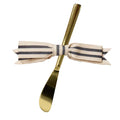 The Gold Spreader Knife & Ribbon by Sophistiplate features a gold butter spreader adorned with a striped beige and black bow around the handle, shown on a white background.