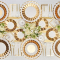 The Gold & White Table Setting by Sophistiplate LLC features gold and white scalloped designer disposable plates, gold cutlery, white napkins, and crystal glasses. Elegant white rose and greenery floral arrangements complete the table decor.