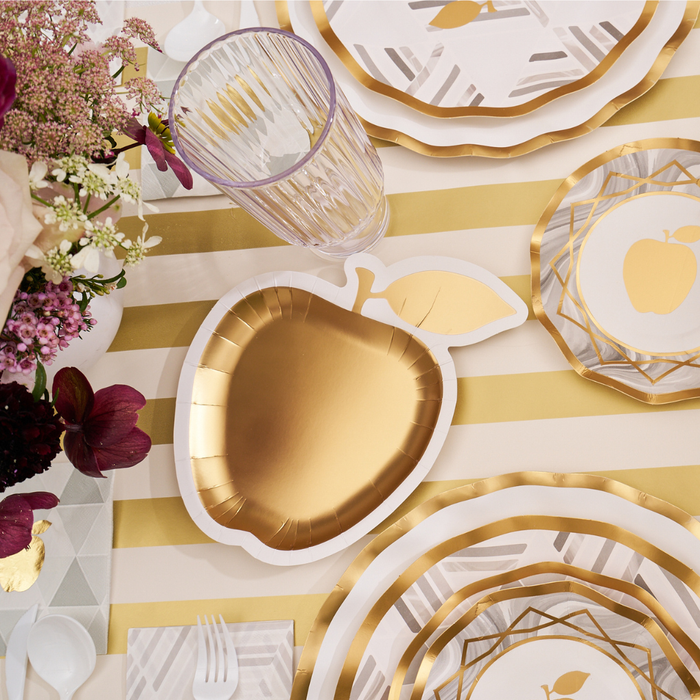 Sophistiplate’s Golden Apple Die-Cut Salad Plates (8pk) from the Golden Apple Table Setting collection are arranged alongside geometric plates on a striped tablecloth, complemented by a glass, utensils, and a bouquet of flowers. Ideal as Rosh Hashanah plates or elegant disposable salad plates, this festive arrangement brings sophisticated flair to any celebration.